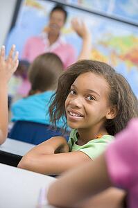 Student in class looking at camera with teacher in background (selective focus)