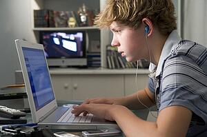 Young boy in bedroom using laptop and listening to MP3 player