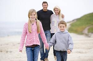 Family walking at beach holding hands smiling
