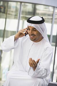 Businessman sitting outdoors by building using cellular phone and smiling (selective focus)