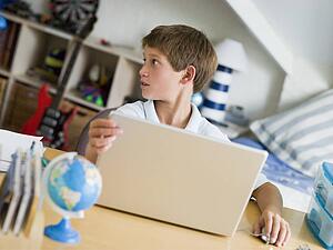 Young Boy Using A Laptop In His Bedroom