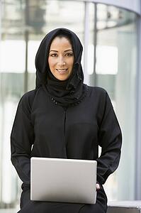 Businesswoman sitting outdoors with laptop by building smiling (selective focus)