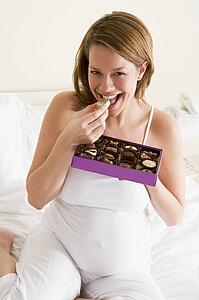 Pregnant woman in bed eating chocolate smiling