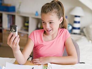 Young Girl Distracted From Her Homework, Playing With A Cellphone