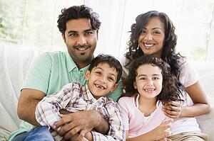 Family in living room sitting on sofa smiling (high key)