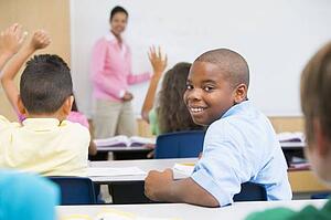 Student in class looking at camera with teacher in background (selective focus)