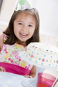 Young girl wearing party hat with birthday cake smiling