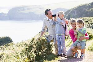 Family on cliffside path using binoculars and smiling