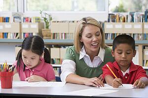 Two students in class writing with teacher helping