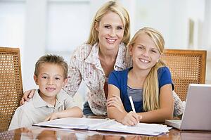Woman helping two young children with laptop do homework in dining room