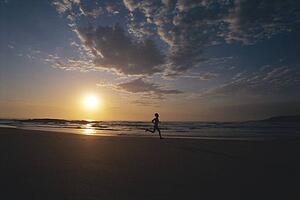 Man outdoors running on a beach at sunset (silhouette)