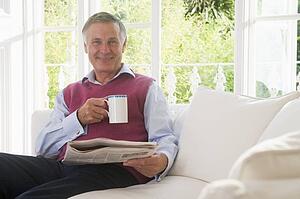 Man in living room with coffee reading newspaper smiling