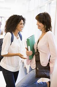 Two women in corridor with books talking (high key)