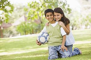 Two young children outdoors in park with ball smiling (selective focus)
