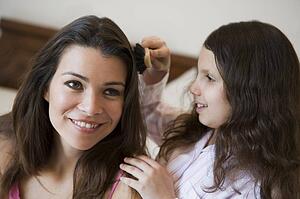 Young girl brushing woman's hair on bed in bedroom smiling (selective focus)