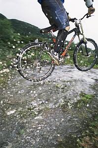 Man outdoors on trails jumping bicycle over puddles (selective focus)