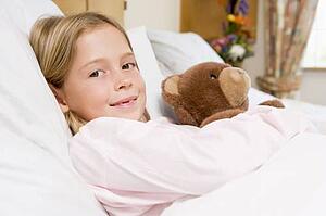 Young Girl Lying In Hospital Bed, Holding Teddy Bear