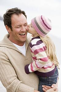 Father holding daughter kissing him at beach smiling