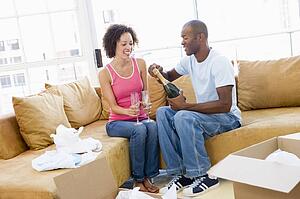 Couple relaxing with champagne by boxes in new home smiling