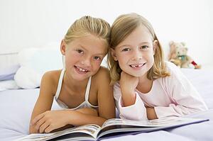 Two Young Girls In Their Pajamas, Reading A Book