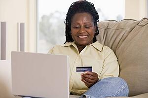 Woman in living room using laptop holding credit card and smiling