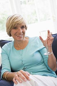 Woman sitting in living room with drink smiling