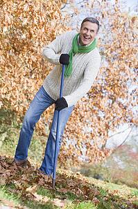Man outdoors raking leaves and smiling (selective focus)