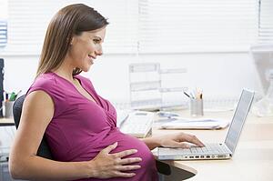 Pregnant woman at work using laptop and smiling