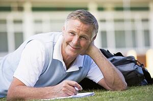 Adult student lying on lawn of school with notebook