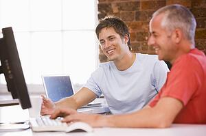 Two businessmen in office typing on computer and smiling