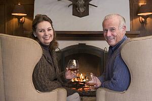Couple sitting in living room by fireplace with drinks smiling