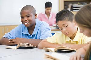 Students in class reading with teacher in background (selective focus)