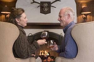 Couple sitting in living room by fireplace with drinks smiling