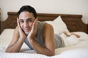 Man relaxing on bed in bedroom smiling (selective focus)