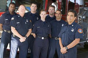 Six firefighters standing in front of fire engine with captain (depth of field)