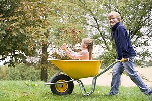 Young boy outdoors pushing young girl in wheelbarrow and smiling (selective focus)