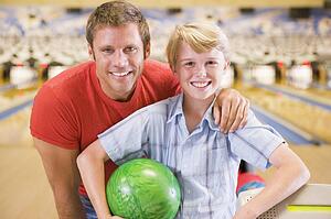 Man and young boy in bowling alley holding ball and smiling