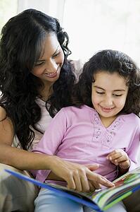 Mother and daughter in living room with book smiling (high key)