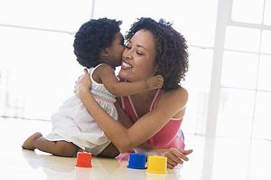 Mother and daughter indoors kissing and smiling