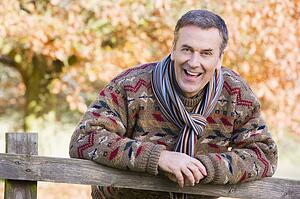 Man outdoors at park leaning on fence smiling (selective focus)