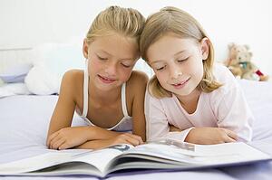 Two Young Girls In Their Pajamas, Reading A Book