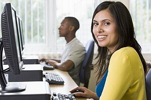 Woman sitting at a computer terminal with man in background (selective focus/high key)
