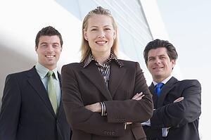 Three businesspeople standing outdoors by building smiling