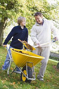 Father and son shoveling leaves into wheelbarrow and smiling (selective focus)