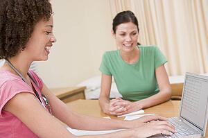 Doctor with laptop and woman in doctor's office smiling
