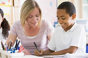 Student in class taking notes with teacher helping