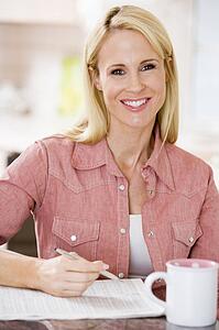 Woman in kitchen with newspaper and coffee smiling