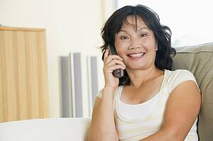 Woman sitting in living room using telephone and smiling