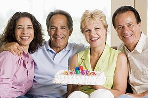 Two couples in living room with cake smiling