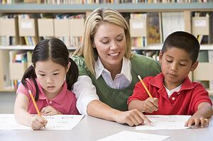 Two students in class writing with teacher helping